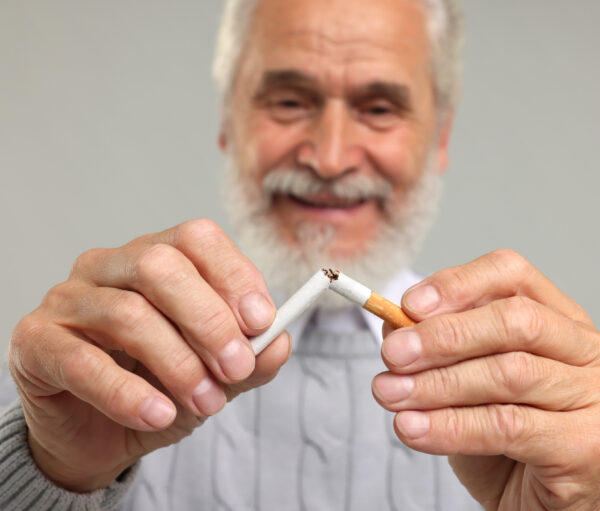 Stop smoking concept. Senior man breaking cigarette on light grey background, selective focus